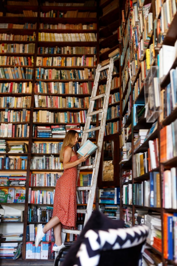 Girl reading book from bookshelves in bookstore,stands on wooden stairs