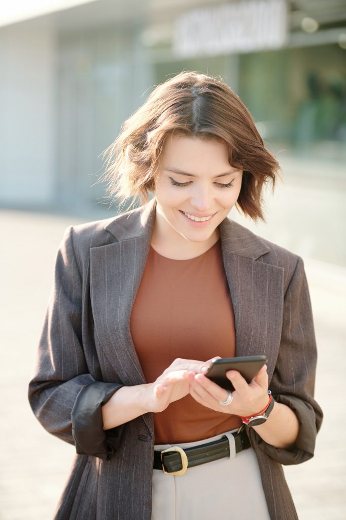 Happy and elegant young businesswoman scrolling through contacts in smartphone