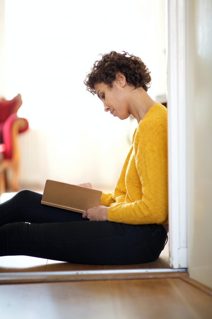 young african american woman sitting on floor with book